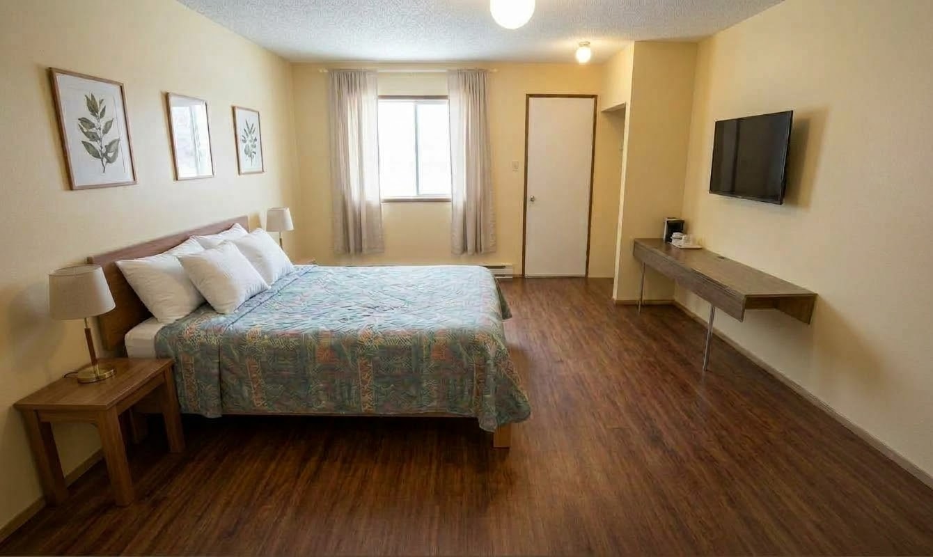 A bright queen room at Pine Creek Motel with one queen bed, a wooden headboard, a wall-mounted TV and a coffee maker on a floating desk